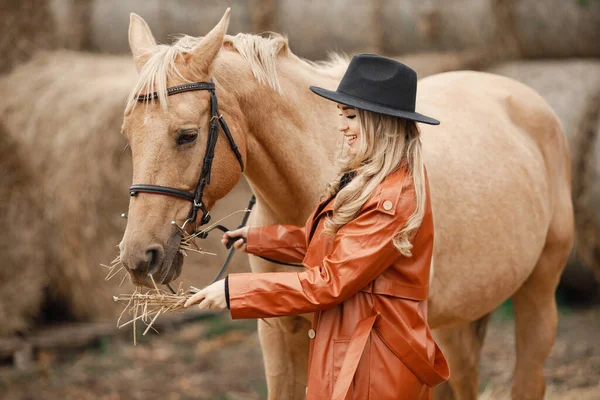 Femme en manteau de cuir rouge touchant un cheval brun sur une ferme — Photo