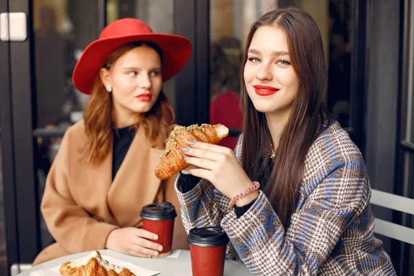 Δύο νεαρά κορίτσια σε υπαίθριο καφέ, πίνοντας καφέ με κρουασάν και κουβεντιάζοντας. — Φωτογραφία Αρχείου