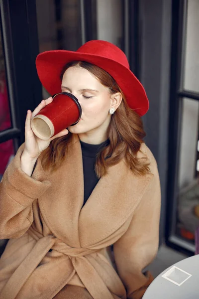 Дівчина з червоним капелюхом сидить у кафе на відкритому повітрі і п'є каву — стокове фото