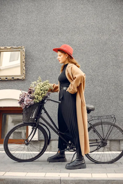 Menina com chapéu vermelho em pé perto de sua bicicleta com uma cesta e flores dentro — Fotografia de Stock