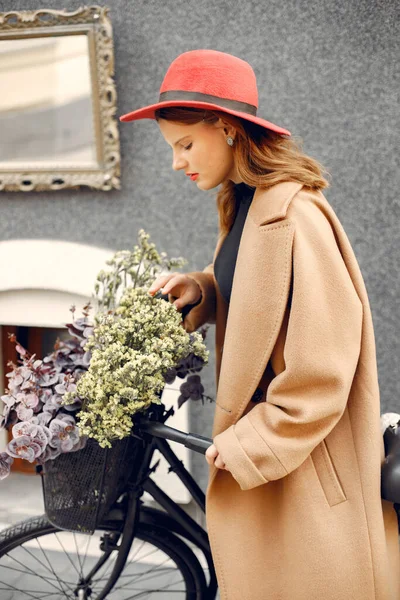 Chica con sombrero rojo de pie cerca de su bicicleta con una cesta y flores en el interior — Foto de Stock