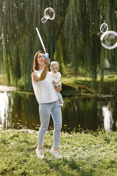 Mladá matka drží svou dcerku v rukou a fouká mýdlové bubliny — Stock fotografie
