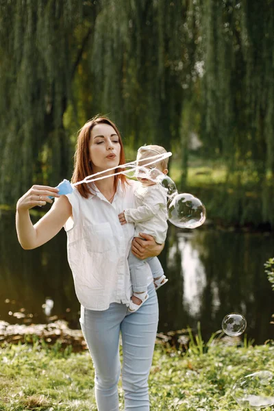 Mladá matka drží svou dcerku v rukou a fouká mýdlové bubliny — Stock fotografie