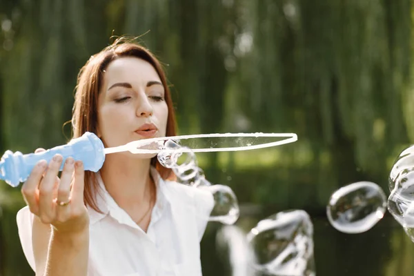 Женщина надувает мыльные пузыри, стоя в парке — стоковое фото