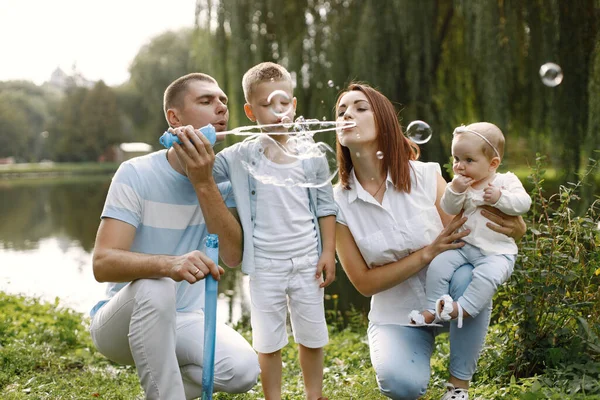 Šťastná rodina foukání mýdlové bubliny v parku u jezera — Stock fotografie