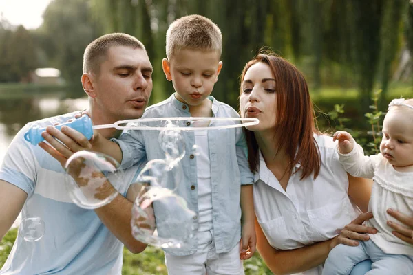 Familia feliz soplando burbujas de jabón en el parque cerca del lago —  Fotos de Stock