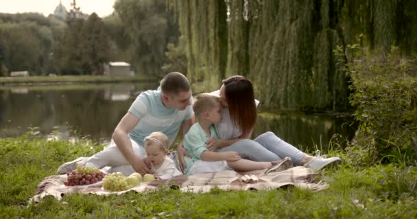 Молодая семья с двумя детьми на открытом воздухе у реки в летний пикник — стоковое видео