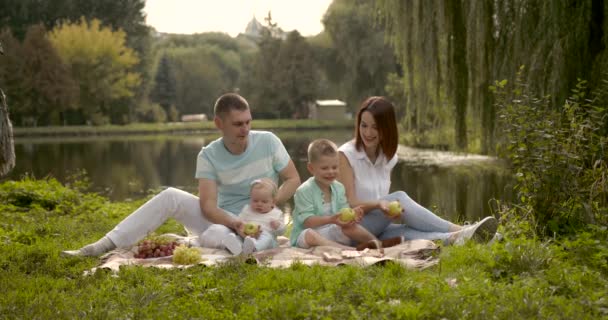 Junge Familie mit zwei Kindern im Freien am Fluss beim sommerlichen Picknick — Stockvideo