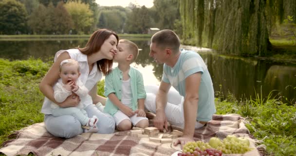 Ung familj med två barn utomhus vid älven på sommaren picknick — Stockvideo