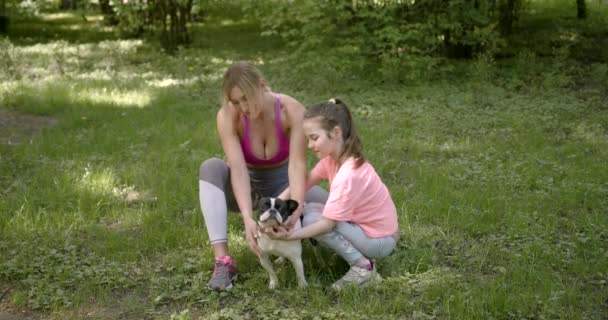 Mor och dotter klappar hunden i en park — Stockvideo