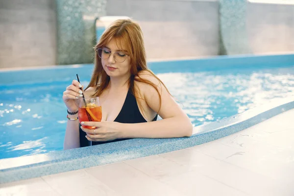 Chica joven en un traje de baño relajarse en una piscina y la celebración de un cóctel —  Fotos de Stock