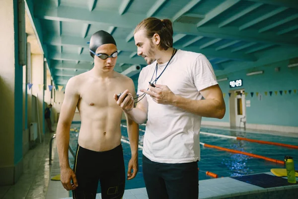 Male coach and swimmer talking by poolside