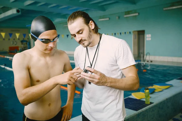 Male coach and swimmer talking by poolside