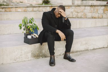 Employee get fired. Black man sitting with box on stairs and regretting.