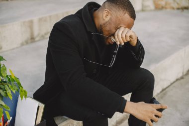 Employee get fired. Black man sitting with box on stairs and regretting.