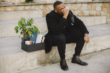 Employee get fired. Black man sitting with box on stairs and regretting.