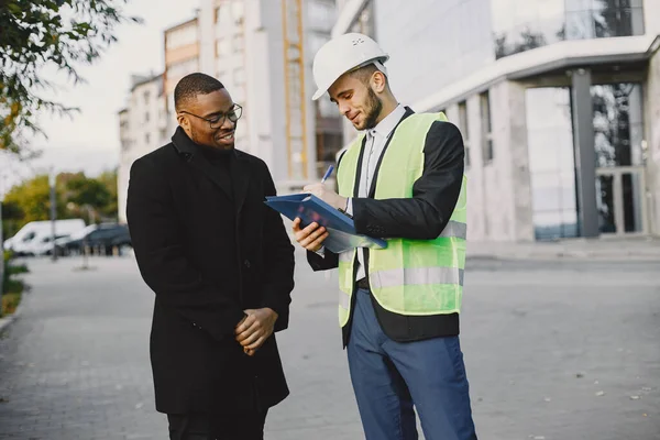 Planning the house. Man in uniform and black customer looking at new built house plan. Buying property, realtor.