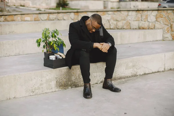 Employee get fired. Black man sitting with box on stairs and regretting.