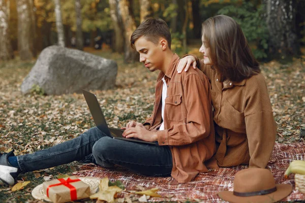 Couple in a park. Guy in a brown shirt. Golden autumn. Man uses a laptop.