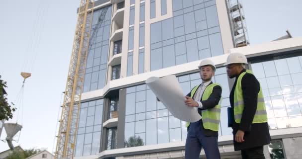 Pracovníci Uniformách Helmách Porovnávají Stavební Plán Blízkosti Nové Budovy Nákresu — Stock video