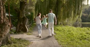 Mutlu aile: anne, baba, çocuklar, oğul ve kız parkta. Çocuk ebeveynlerinin elini tutuyor. Annesinin kollarında küçük bir kız