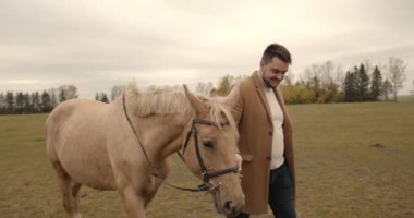 Man guiding horse with lead rope through field. Animal and people, friendship.