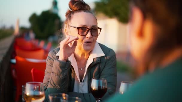 Зрелая женщина в очках сидит в кафе со своей дочерью и пьет вино — стоковое видео