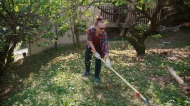 Yetişkin bir kadın çimenlikten kuru yaprakları tırmıkla temizliyor.