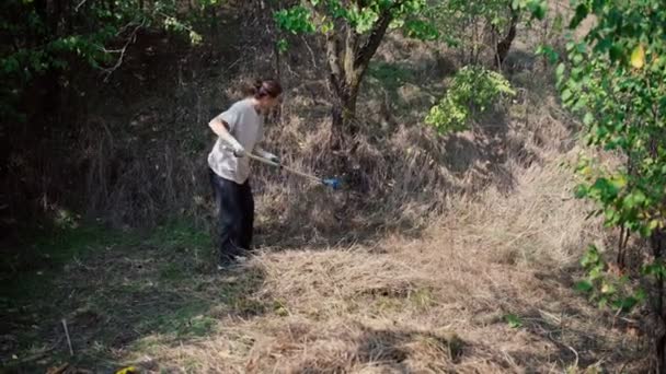 Een jonge vrouw ruimt het droge gras op met een hark — Stockvideo
