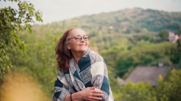 Een volwassen vrouw die in een deken staat en geniet van het uitzicht — Stockvideo