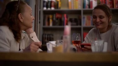 Yetişkin bir kadın yetişkin kızıyla bir kafede oturur.,