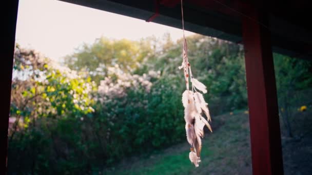 En stickad drömfångare med fjädrar och stenar hänger på verandan — Stockvideo