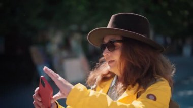 Yetişkin bir kadın şehirde yürürken telefonuyla video görüşmesi yapıyor.