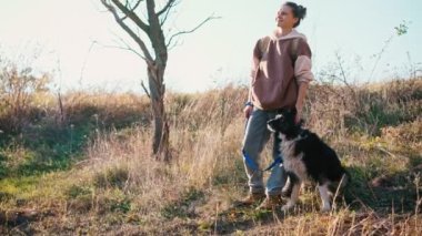 Genç bir kadın parkta yürürken sevimli köpeğini okşuyor.