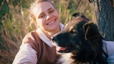 Tüylü köpeğini okşayan ve kameraya bakan genç bir kadının portresi.
