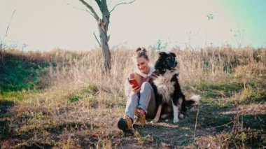 Genç yetişkin bir kadın köpeğiyle yürürken telefonunu kullanıyor.