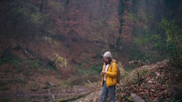 Una giovane donna con uno zaino usando il suo telefono mentre in piedi al lago foresta — Video Stock