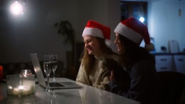 Noel şapkalı iki güzel genç kadın, bir dizüstü bilgisayarla görüntülü arama yapıyorlar.