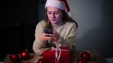 Noel şapkalı genç bir kadın akıllı telefon ekranına bakıyor.