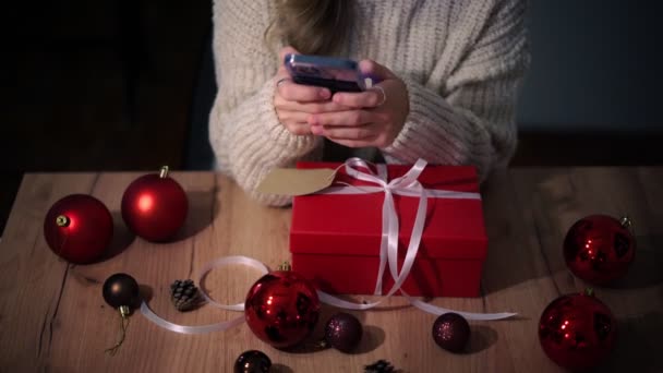 Frauenhände mit einem Smartphone, das ein verpacktes Neujahrsgeschenk fotografiert. — Stockvideo