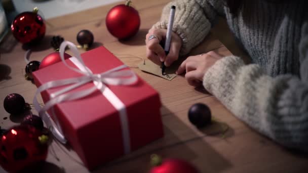 Primer plano de las manos femeninas escribiendo un mensaje de felicitación en la etiqueta de regalo. — Vídeos de Stock