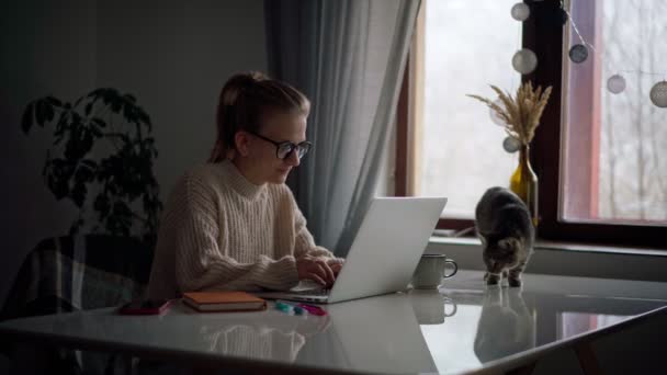 Una joven escribiendo en un ordenador portátil mientras trabaja o estudia desde casa — Vídeos de Stock