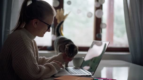 Una joven escribiendo en un ordenador portátil mientras trabaja o estudia desde casa — Vídeos de Stock
