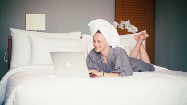 Nainen aamutakissa ja pyyhe päässään katsoo kannettavan tietokoneen näyttöä. — kuvapankkivideo