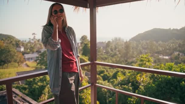 A young adult woman talking on her phone while standing on a terrace with a view — Video Stock