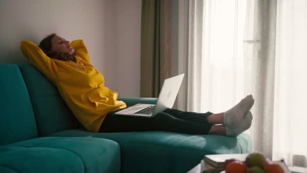 A young woman is relaxing reclining on the couch with a laptop on her lap — 비디오