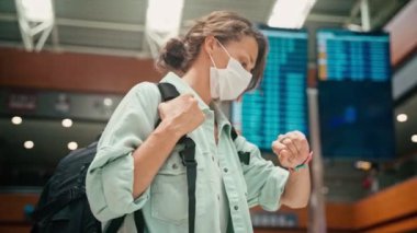A young woman in a mask looking at her watch while at the airport