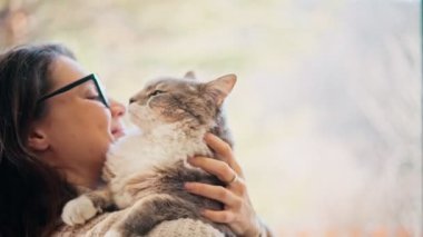 A young woman petting her cat while holding him in her arms