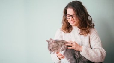 A woman petting her cute gray fluffy cat while holding him in her arms.