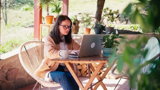 En ung kvinna frilansar arbetar på sin laptop medan hon sitter på terrassen — Stockvideo